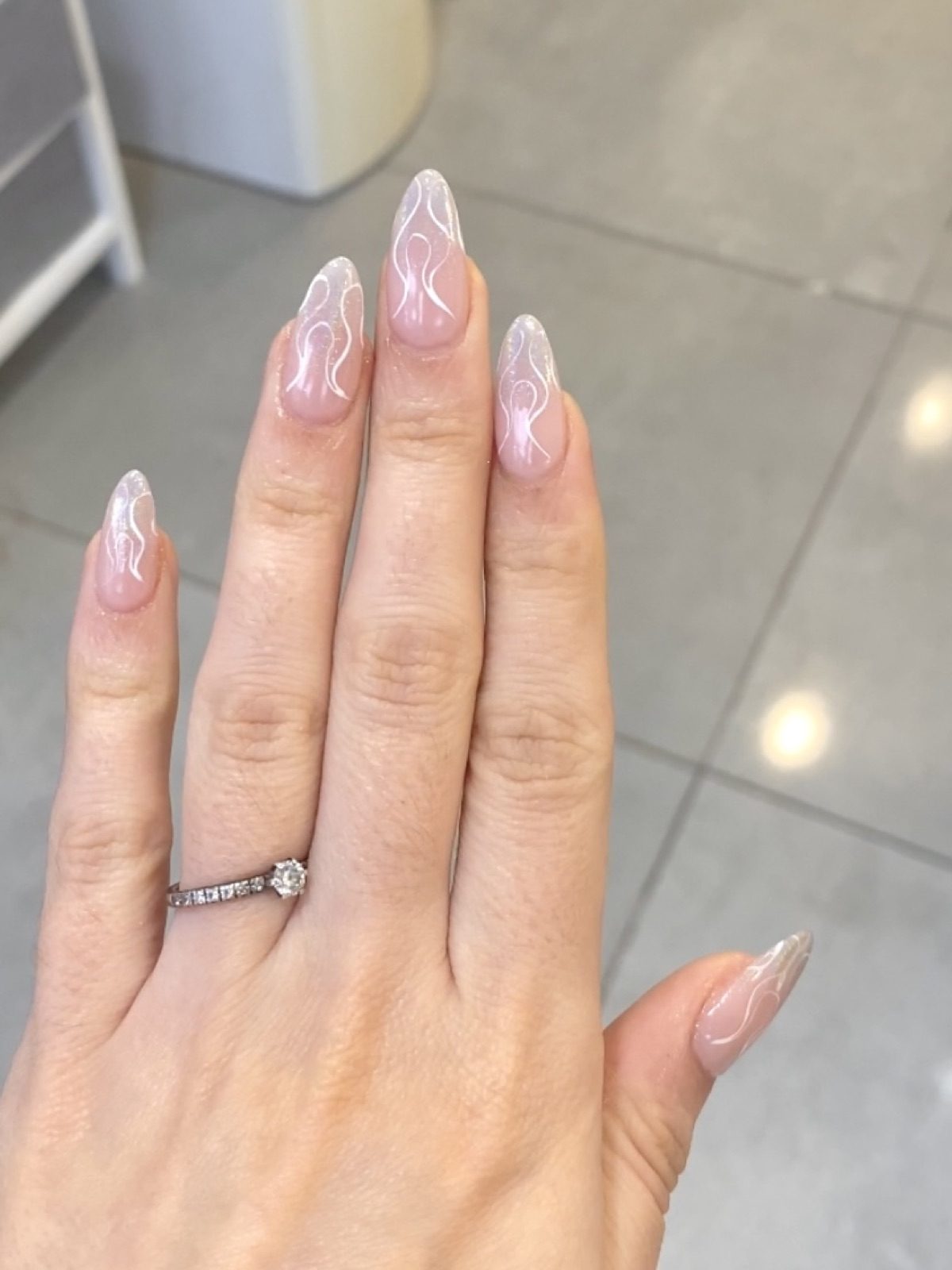 Sheer almond nails with fine white swirl line art, hand held over a pale concrete floor