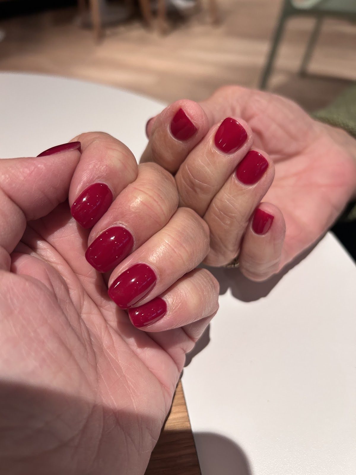A fresh set of glossy deep-red almond nails resting on a table