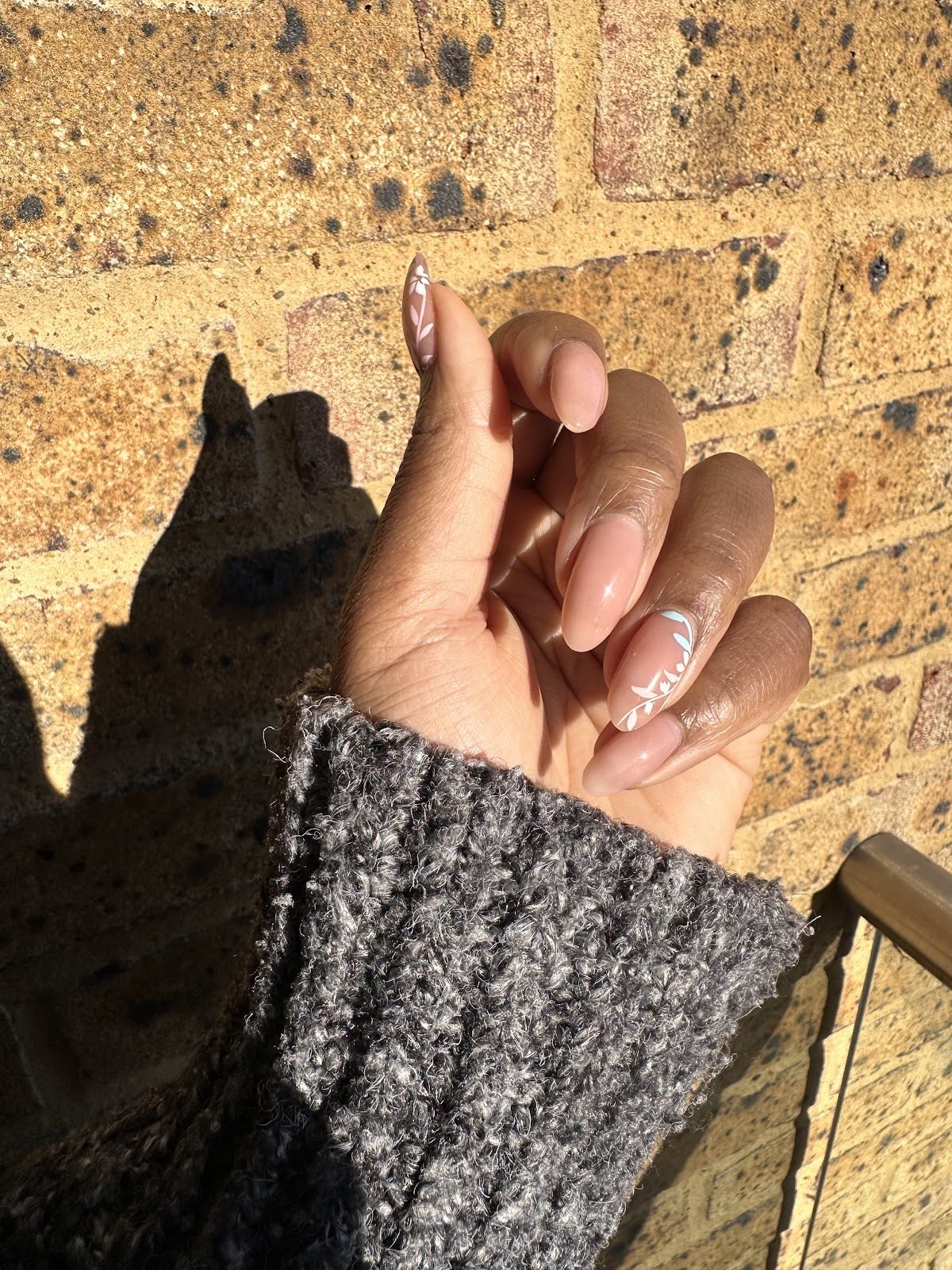 Long nude nails with a subtle chrome and glitter accent against a sunlit brick wall
